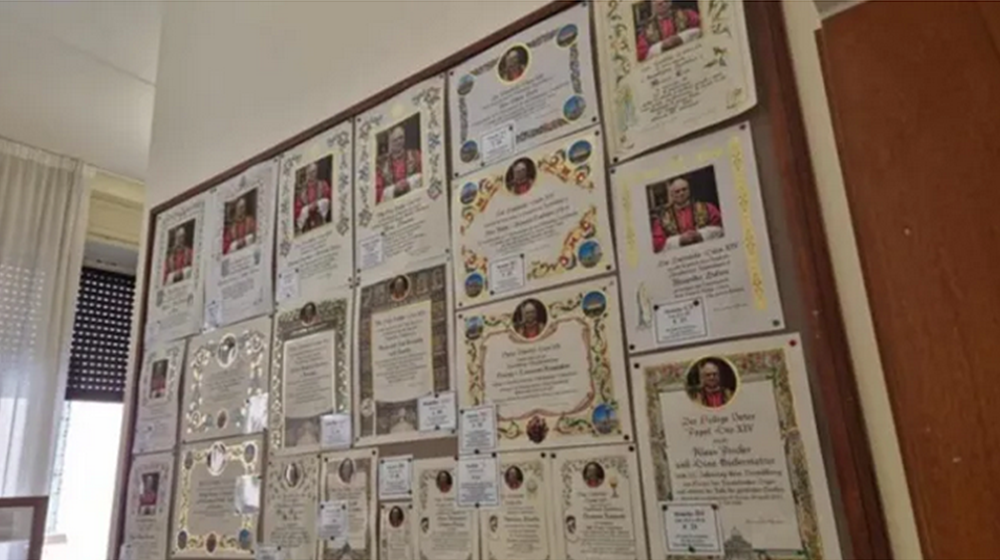 Placas penduradas no escritório da caridade papal na Cidade do Vaticano mostram diferentes modelos de certificados de bênção papal que podem ser encomendados. | Hannah Brockhaus/CNA Placas penduradas no escritório da caridade papal na Cidade do Vaticano mostram diferentes modelos de certificados de bênção papal que podem ser encomendados. | Hannah Brockhaus/CNA